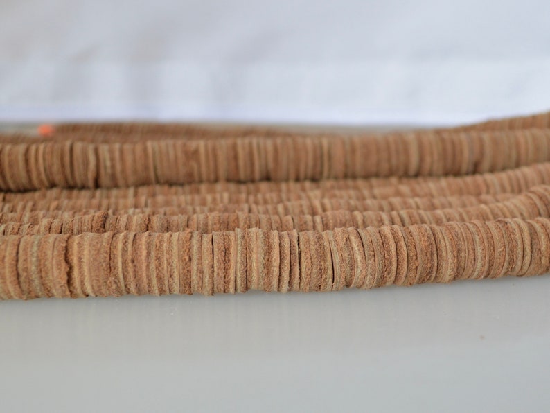 Op de afbeelding: Een close-up van een stapel bruin lederen koord, gesneden in kleine cirkels. Het koord is gerangschikt in rijen, waardoor een textuurpatroon ontstaat.