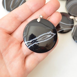 May include: Black and white agate pendant with a silver bail. The pendant is round and has a smooth, polished surface. The agate has a natural pattern of white lines on a black background.
