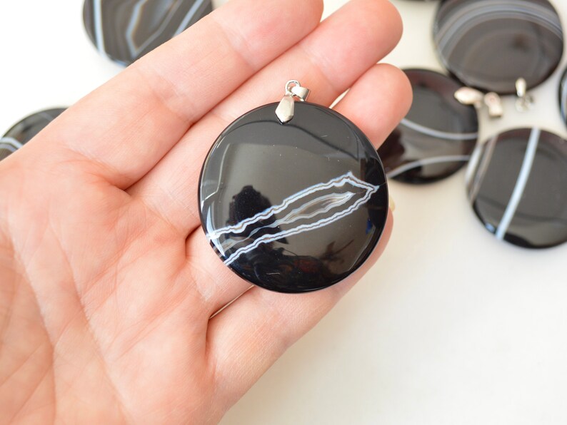May include: Black and white agate pendant with a silver bail. The pendant is round and has a smooth, polished surface. The agate has a natural pattern of white lines on a black background.
