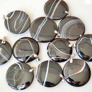 May include: Ten black and white agate pendants with silver jump rings. The pendants are round and have a polished finish.