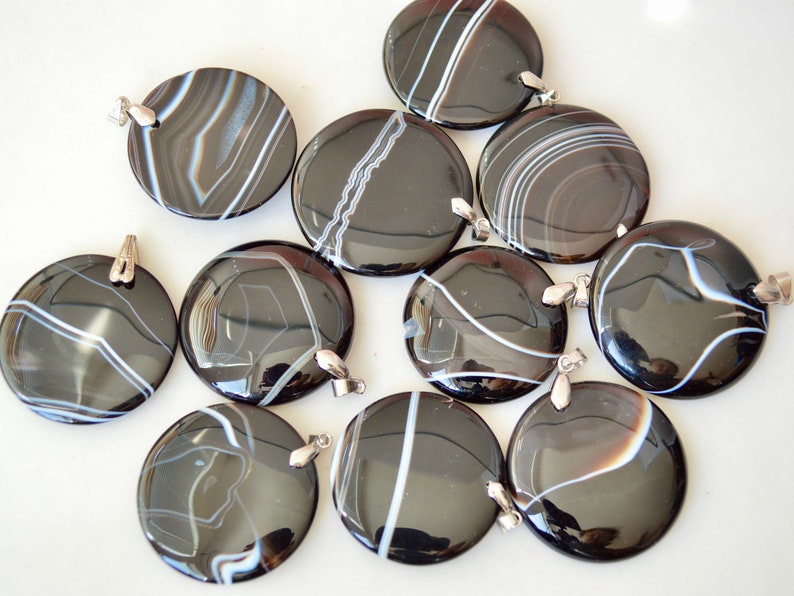 May include: Ten black and white agate pendants with silver jump rings. The pendants are round and have a polished finish.