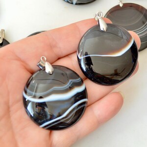 May include: Two black and white agate pendants with silver bail. The pendants are round and have a polished finish. The agate has white stripes on a black background.