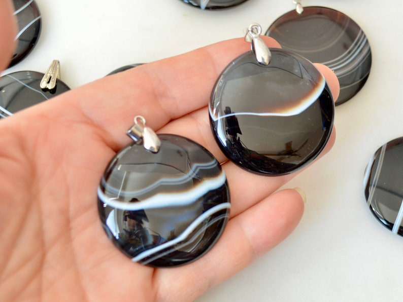 May include: Two black and white agate pendants with silver bail. The pendants are round and have a polished finish. The agate has white stripes on a black background.