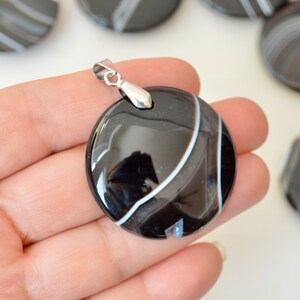 May include: Black and white agate pendant with a silver bail. The pendant is round and has a smooth, polished finish.