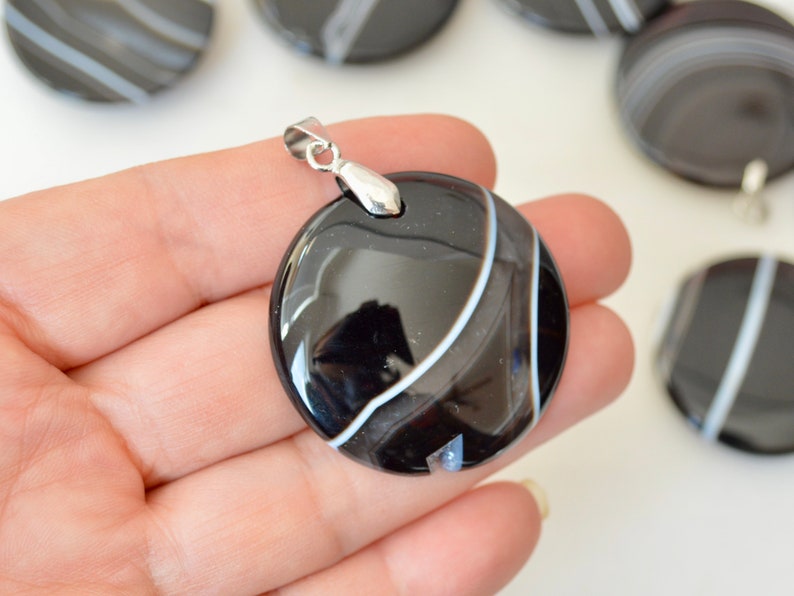 May include: Black and white agate pendant with a silver bail. The pendant is round and has a smooth, polished finish.
