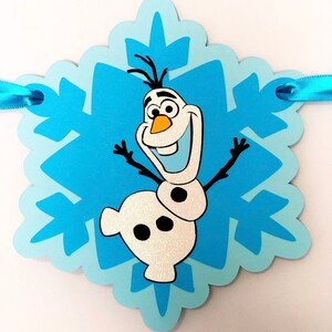 Pu&ograve; includere: Uno striscione a forma di fiocco di neve azzurro con il personaggio Olaf del film Frozen. Olaf sorride con le braccia tese. Lo striscione ha un nastro azzurro per appenderlo.