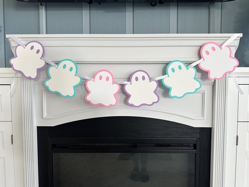 Op de afbeelding: Een witte spookbanner met pastelroze, blauwe en paarse accenten. De banner hangt boven een open haard.