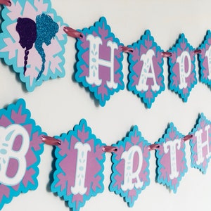 Pu&ograve; includere: Uno striscione decorativo con le parole "HAPPY BIRTHDAY" in bianco, su un disegno a fiocco di neve viola e blu. Lo striscione &egrave; infilato con un nastro rosa e presenta una silhouette di due figure.