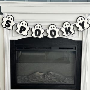 Op de afbeelding: Een zwart-witte spookbanner met het woord "SPOOKY" erop. De banner hangt boven een zwarte open haard.