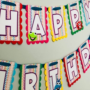 May include: A colorful Happy Birthday banner with each letter on a separate flag. The flags are decorated with a rainbow pattern and feature cartoon characters.