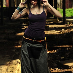 May include: A person wearing a rainbow-colored hat with a purple top and gray pants. The hat has a unique design with curved horns and a rainbow gradient. The outfit includes a dark purple tank top, gray harem pants, and blue sneakers.