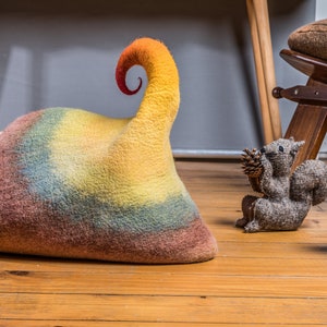 May include: A colorful felt mushroom, squirrel, and a rainbow-colored felt hat with a curled top. The items are on a wooden floor.