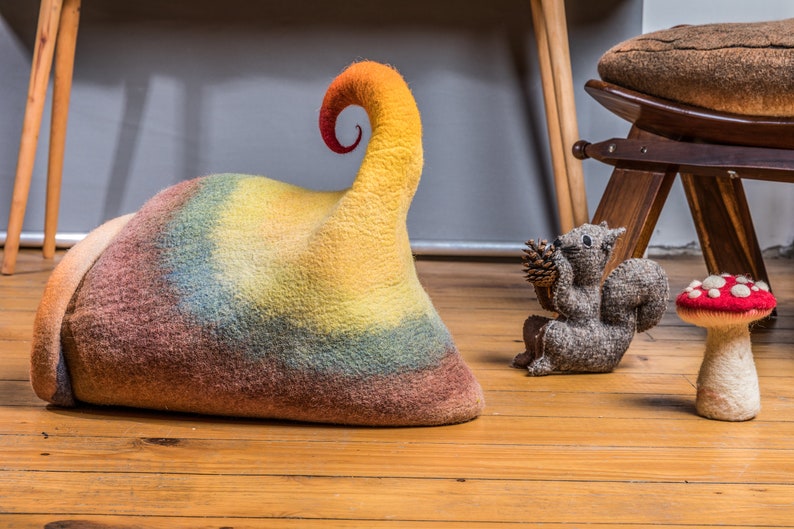 May include: A colorful felt mushroom, squirrel, and a rainbow-colored felt hat with a curled top. The items are on a wooden floor.