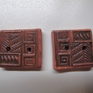 May include: Two square ceramic buttons with a geometric pattern in shades of brown and pink.