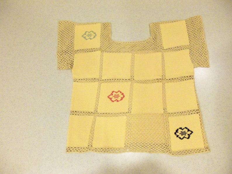 May include: A patchwork top in a combination of yellow squares and open-weave beige sections. The top has short sleeves and is decorated with embroidered floral designs in blue, red, and black. The garment is a unique, handcrafted piece, likely a summer top.