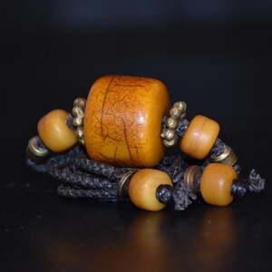 Könnte beinhalten: Nahaufnahme einer Halskette mit einer großen Bernsteinperle und kleineren Bernsteinperlen. Die Halskette ist aus einem dunkelbraunen Band und Messingakzenten gefertigt.