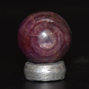 Könnte beinhalten: Eine rosa und violette Edelsteinkugel mit einem wirbelnden Muster, auf einem grauen Ständer ausgestellt.