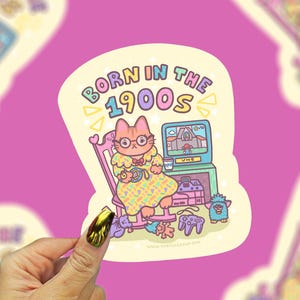 May include: A die-cut sticker featuring a cartoon cat wearing glasses and a yellow patterned dress, sitting in a pink rocking chair. The text reads BORN IN THE 1900S above a television, a video game console, a VHS tape, and various retro toys.