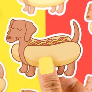 May include: A brown dachshund dog wearing a yellow hot dog costume with mustard and ketchup. The dog is wearing a smile and has its eyes closed. The hot dog costume has the word "Sausage" written on it.