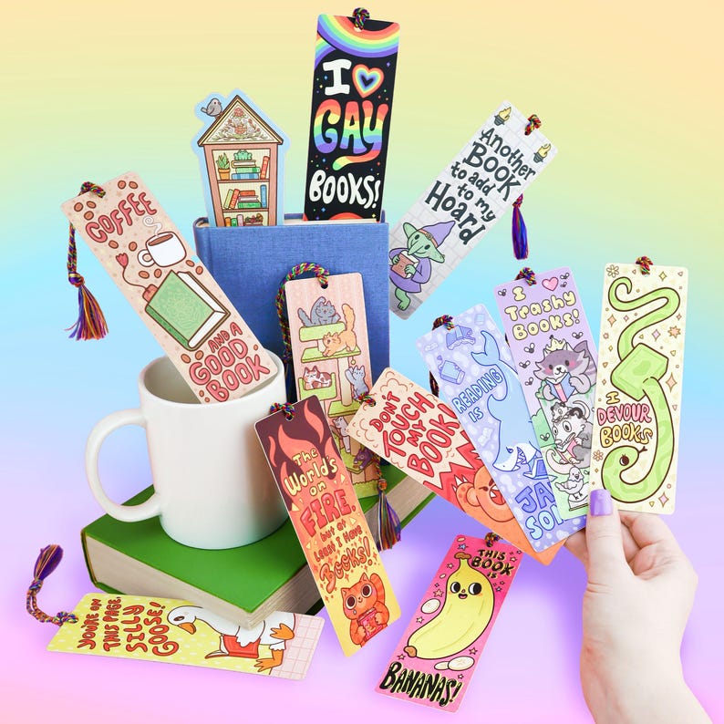May include: A collection of colorful, illustrated bookmarks with various designs and text, including "I ♡ GAY BOOKS!", "Coffee and a Good Book", and "Bananas!". Some bookmarks have tassels.