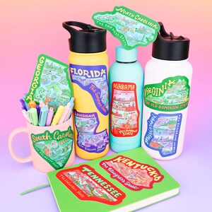 Puede incluir: Surtido de pegatinas de colores en forma de estado que presentan los contornos de cada estado y varios puntos de referencia. Las pegatinas se colocan en una variedad de art&iacute;culos, que incluyen una taza, botellas de agua y un cuaderno.