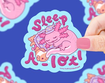 Könnte beinhalten: Ein rosa Axolotl mit einer blauen und weißen Schlafkappe liegt auf einem rosa und violetten Kissen und schläft. Das Axolotl ist von rosa und weißen Herzen und einem kleinen rosa und weißen Teddybär umgeben. Der Text "Sleep a lot!" ist in rosa Buchstaben auf blauem Hintergrund geschrieben. Der Text "www.turtlesoup.com" ist in weißen Buchstaben auf blauem Hintergrund geschrieben.
