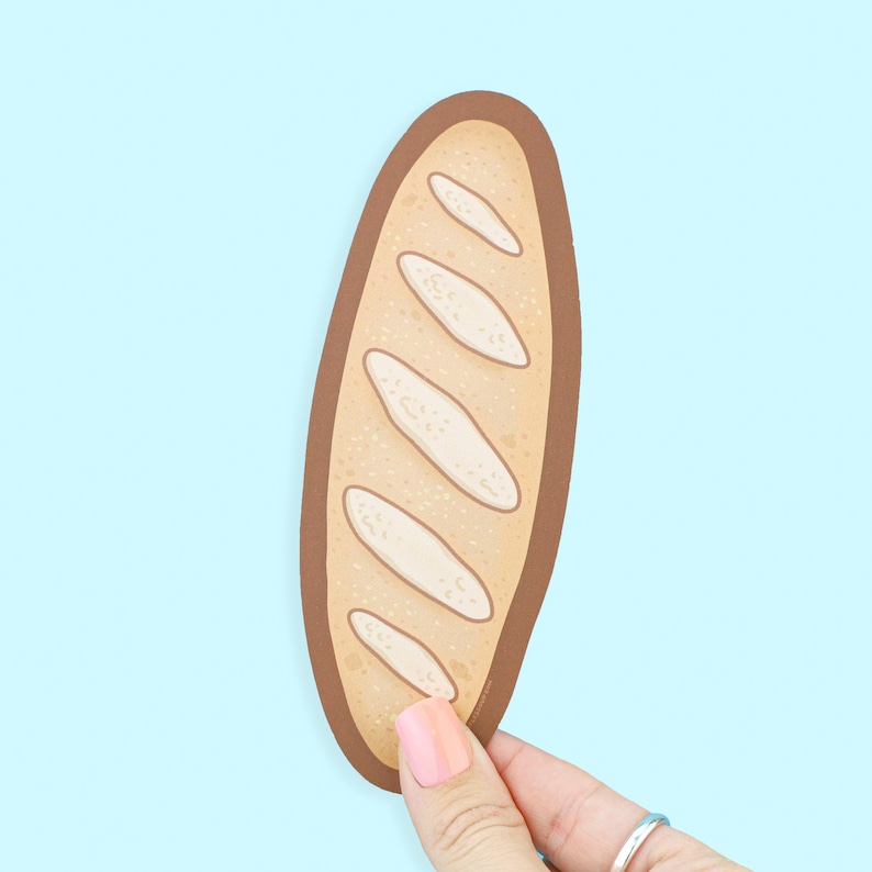 May include: A cartoon illustration of a baguette, featuring a light brown crust and off-white interior. The bread is held against a light blue background. The design includes details like the characteristic cuts on the bread's surface.