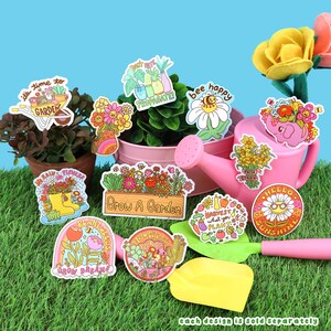 May include: A set of 10 colorful illustrated stickers with gardening themes. The stickers feature phrases like "It's time to garden", "Plant seeds", "Grow dreams", "Bee happy", "Don't hate propagate", "Harvest what you plant", "Bloom where you're planted", "No rain, no flowers", "Hello sunshine", and "Grow a garden".