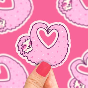 May include: Pink sloth sticker with a heart-shaped outline. The sloth is holding a pink heart in its arms. The sticker has a white outline and the text "TURTLES SOUP" in the bottom right corner.