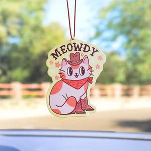 May include: A yellow car air freshener with a cartoon cat wearing a cowboy hat and bandana. The text "MEOWDY" is written above the cat.