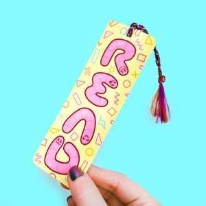 May include: A yellow bookmark with pink worms forming the word "REMS" on a bright blue background. The bookmark has a colorful tassel.