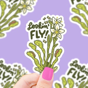 May include: A white sticker with a green cartoon illustration of a Venus flytrap with white flowers and the text "Lookin' Fly!"