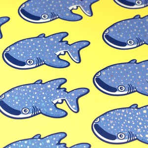 May include: A set of six blue and white whale shark stickers with a glittery finish. The stickers feature a cartoon whale shark with white spots and a light blue background. The stickers are perfect for adding a touch of whimsy to your laptop, water bottle, or planner.