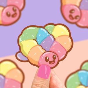 May include: A rainbow-colored donut with a smiling face. The donut is made of pastel pink, blue, yellow, and green frosting. The donut is being held by a hand.