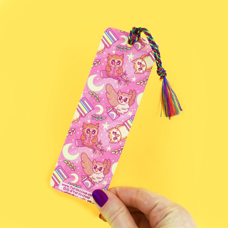 Pu&ograve; includere: Segnalibro rosa con un motivo ripetitivo di gufi che leggono libri. I gufi sono marroni e bianchi con accenti rosa. Il segnalibro ha un fiocco arcobaleno.
