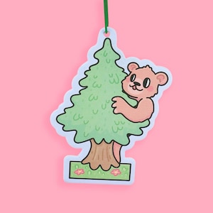 May include: A brown bear hugging a green pine tree with a brown trunk. The tree is on a blue and green base with pink flowers.