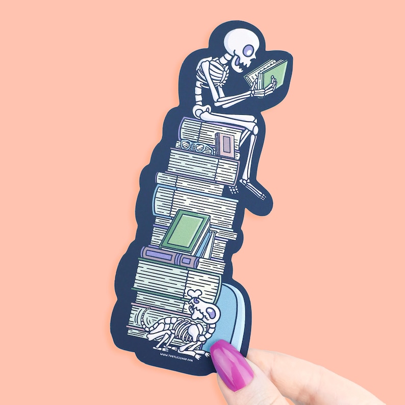 May include: A sticker depicting a skeleton reading a book while seated on a pile of books. The skeleton is white, and the books are various shades of green, purple, and white. A skeleton dog is at the base.