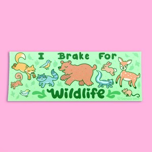 May include: Green sticker with the text "I Brake For Wildlife" in green letters. The sticker features a variety of animals including a bear, deer, fox, raccoon, squirrel, rabbit, and birds on a green background with leaves.