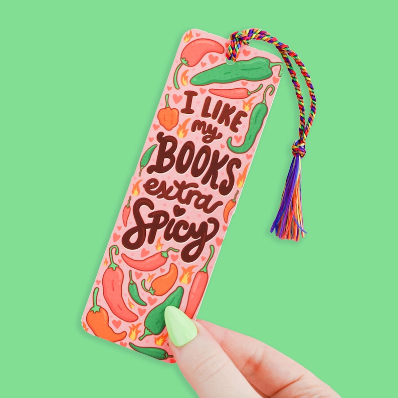 May include: Pink bookmark with a chili pepper theme. It says "I like my books extra spicy" with a red heart and flames.