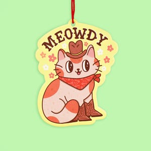 May include: A yellow and white ornament with a cartoon cat wearing a cowboy hat and bandana. The cat is sitting down with its legs crossed. The ornament says "MEOWDY" in a western font.