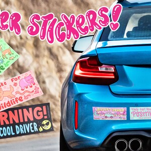 May include: A blue car with a variety of bumper stickers. The stickers feature illustrations of animals, a warning about a super cool driver, and a message about positivity. The license plate reads "Tintles Soup" and "STICKER".