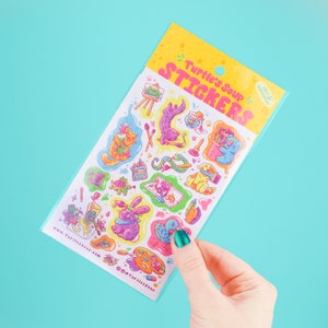 May include: A sheet of colorful stickers featuring cute animal illustrations with a whimsical art theme. The stickers are packaged in a clear plastic bag with a yellow header that reads "Turtle's Soup Stickers".