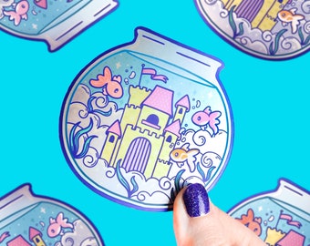May include: A sticker of a blue fishbowl with a pink and yellow castle inside. There are three gold fish swimming around the castle. The fishbowl is surrounded by white clouds.