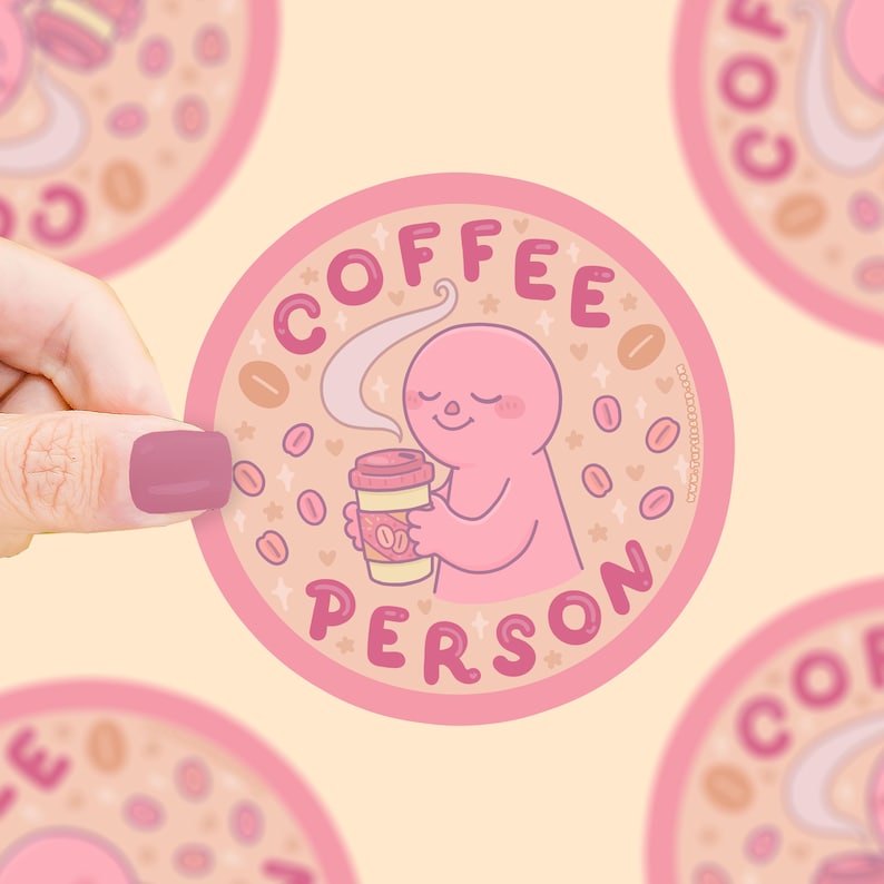 Puede incluir: Una pegatina redonda con borde rosa y las palabras "COFFEE PERSON" en rosa. Presenta una figura de dibujos animados rosa sosteniendo una taza de caf&eacute;, rodeada de granos de caf&eacute; y estrellas. El fondo es de color melocot&oacute;n claro.