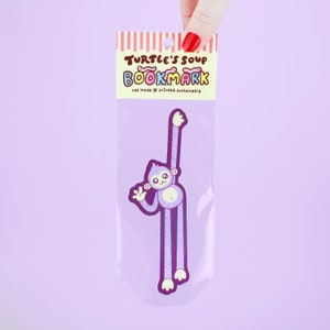 Puede incluir: Marcap&aacute;ginas de mono morado con el texto "Turtle's Soup Bookmark" y "usa made &hearts; printed sustainably".