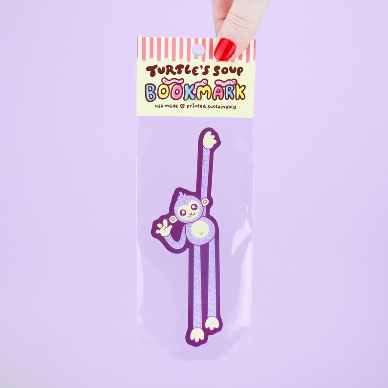 Puede incluir: Marcap&aacute;ginas de mono morado con el texto "Turtle's Soup Bookmark" y "usa made &hearts; printed sustainably".