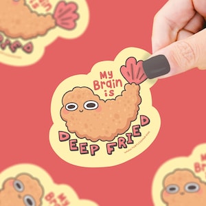 May include: A yellow sticker featuring a cartoon shrimp. The shrimp is light brown with a pink tail and a smiling face. The text "My Brain is Deep Fried" is written on the sticker.