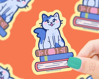 May include: A blue and white cat sitting on a stack of three books. The books have different colored covers and the top book has the text "www.turtlesoup.com" printed on it.