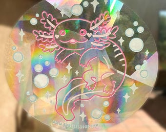 Könnte beinhalten: Ein holografischer Aufkleber mit einem rosa Axolotl mit weißem Umriss. Der Axolotl ist von weißen Blasen und Sternen umgeben. Der Aufkleber hat eine regenbogenfarbene, irisierende Oberfläche und den Text "www.turtle3soup.com" unten.