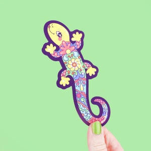 May include: A colorful, patterned lizard sticker with a yellow body and purple outline. The lizard has a whimsical, cartoon-like design with pink, blue, and green floral details.
